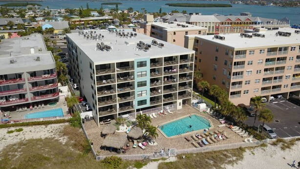 A multi-story hotel with a rooftop pool, a smaller pool, and a beach area with lounge chairs.