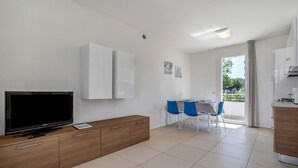 Un salon moderne avec un téléviseur à écran plat, un meuble en bois et un coin repas avec des chaises bleues.