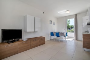 A modern living room with a flat-screen TV, wooden cabinet, and a dining area with blue chairs.