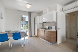 A modern kitchen with white cabinets, a microwave, and a dining area with blue chairs.