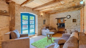 Une pièce rustique aux murs de pierre, avec des poutres en bois, une porte bleue et un coin salon confortable, comprenant des canapés et une petite table.