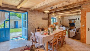 Un coin repas rustique avec une table et des chaises en bois, un mur en pierre et une porte bleue donnant sur l’extérieur.