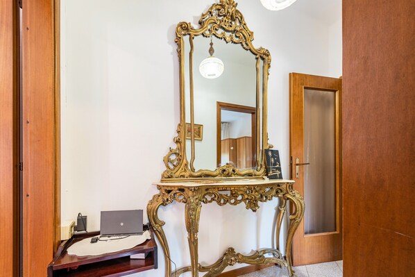 A room with a wooden door, a mirror on a table, a laptop, and a small table with a tissue box.