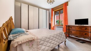 Una camera da letto con un letto, una cassettiera, una televisione e una finestra con tende.