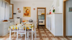 Un coin repas avec une table dressée pour quatre personnes, une cuisine en arrière-plan et un tableau accroché au mur.