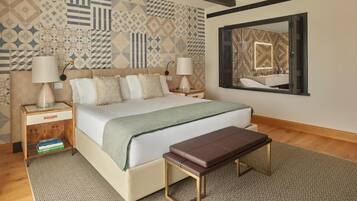 Un dormitorio con cama, mesitas de noche, una banca, alfombra estampada y un espejo en la pared.
