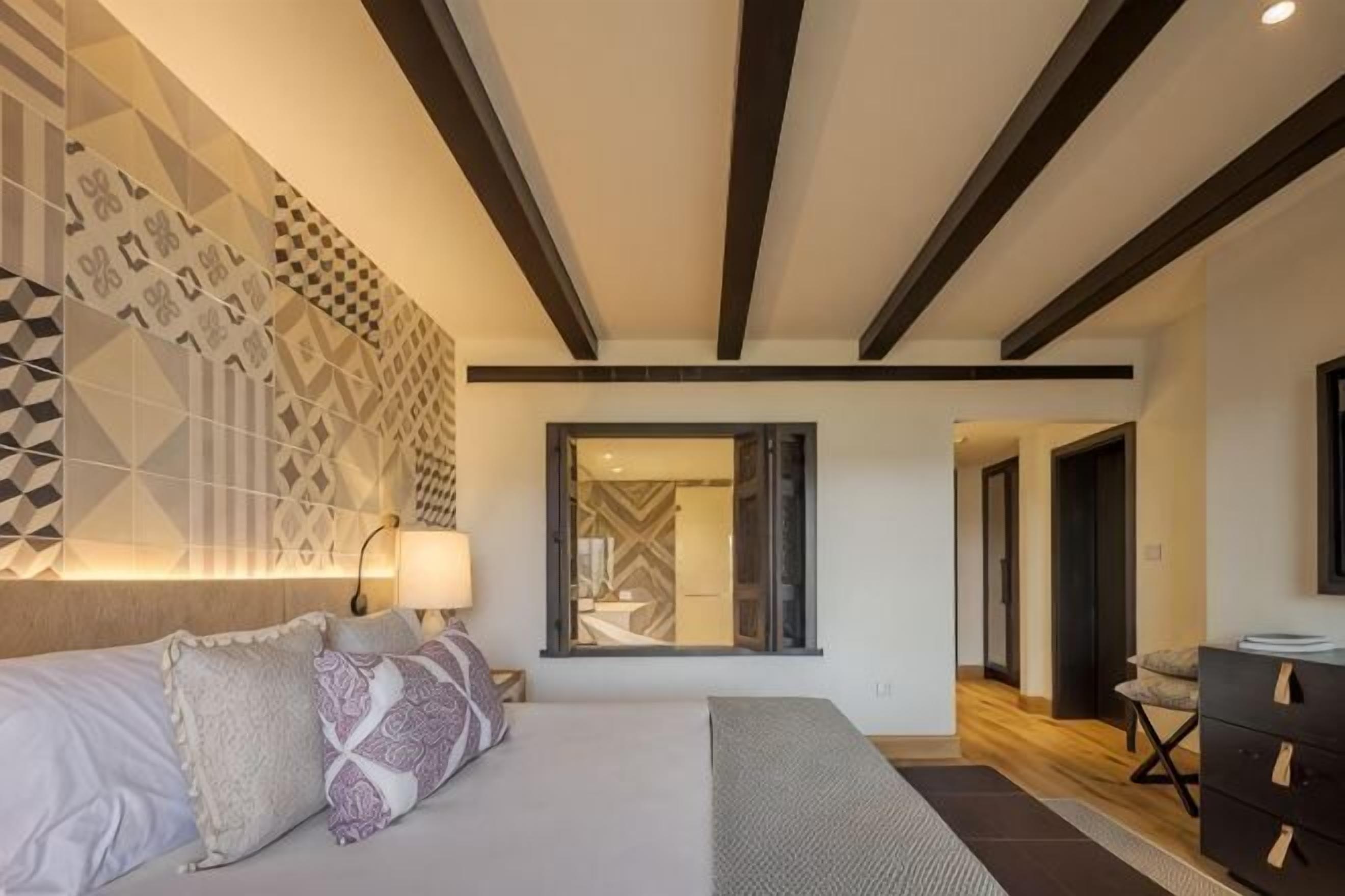 A bedroom with a bed, bedside table, lamp, and a geometric-patterned wall.