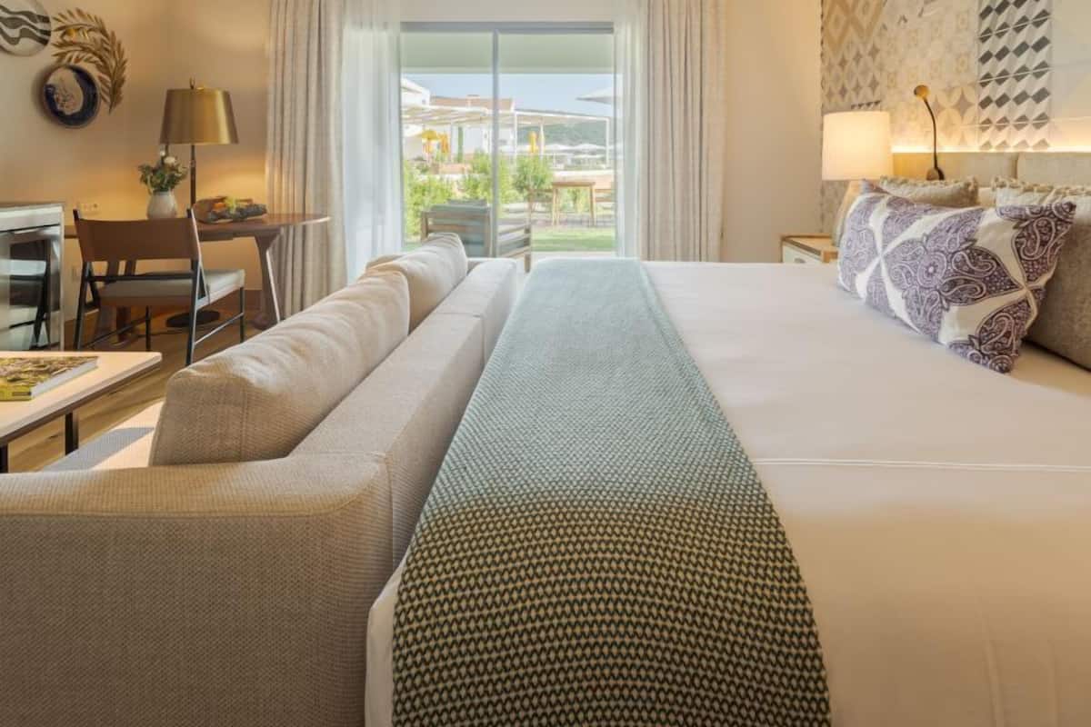 A hotel room with a large bed, a sofa, a desk, and a view of the outdoors.