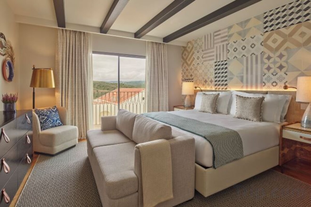 A hotel room with a large bed, a sofa, a desk, and a view of the outdoors.