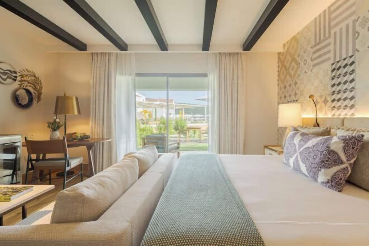 A hotel room with a large bed, a sofa, a desk, and a view of the outdoors.