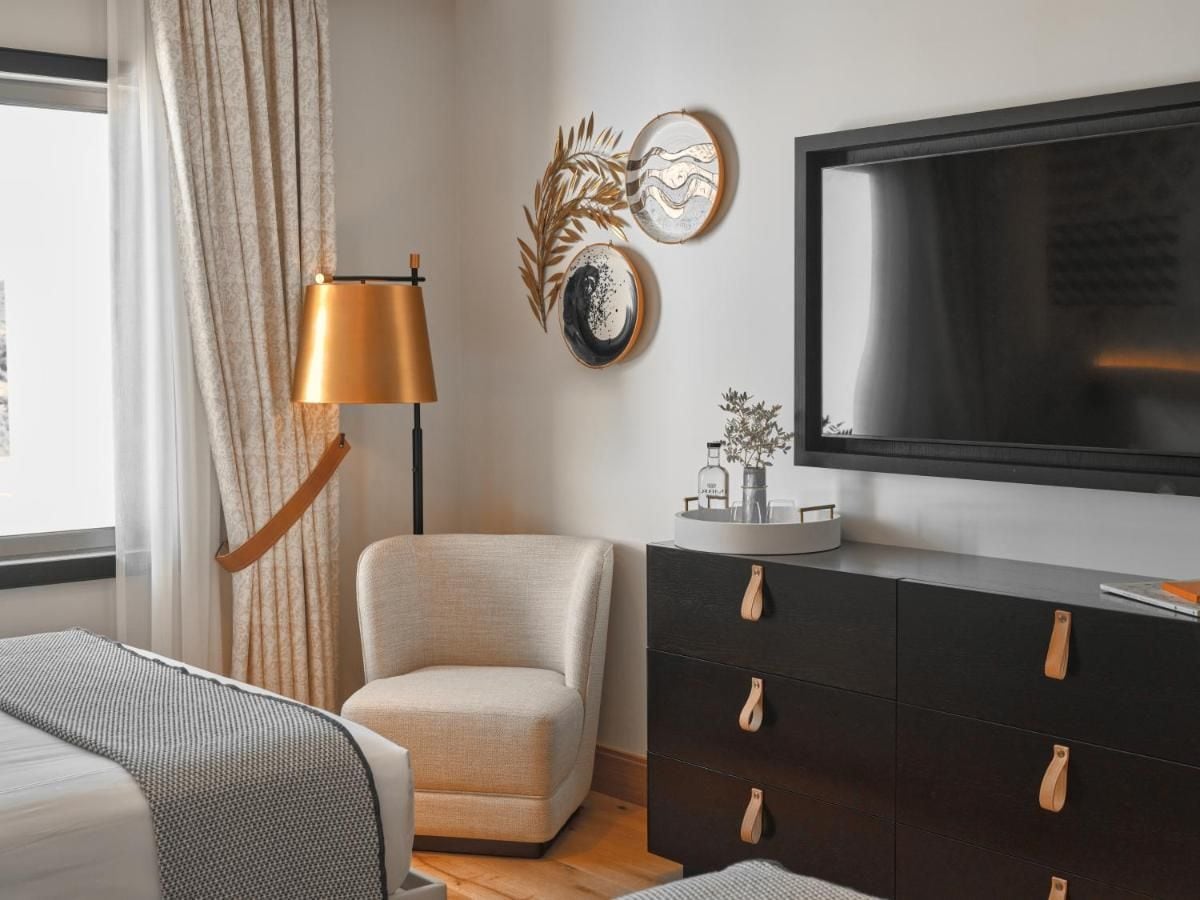 Quarto moderno com televisão de tela plana grande, sofá, poltrona, cômoda com gavetas e luminária de chão.