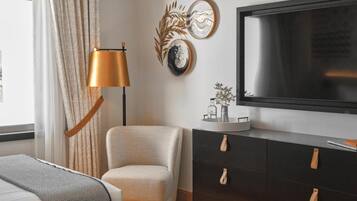 Quarto moderno com televisão de tela plana grande, sofá, poltrona, cômoda com gavetas e luminária de chão.