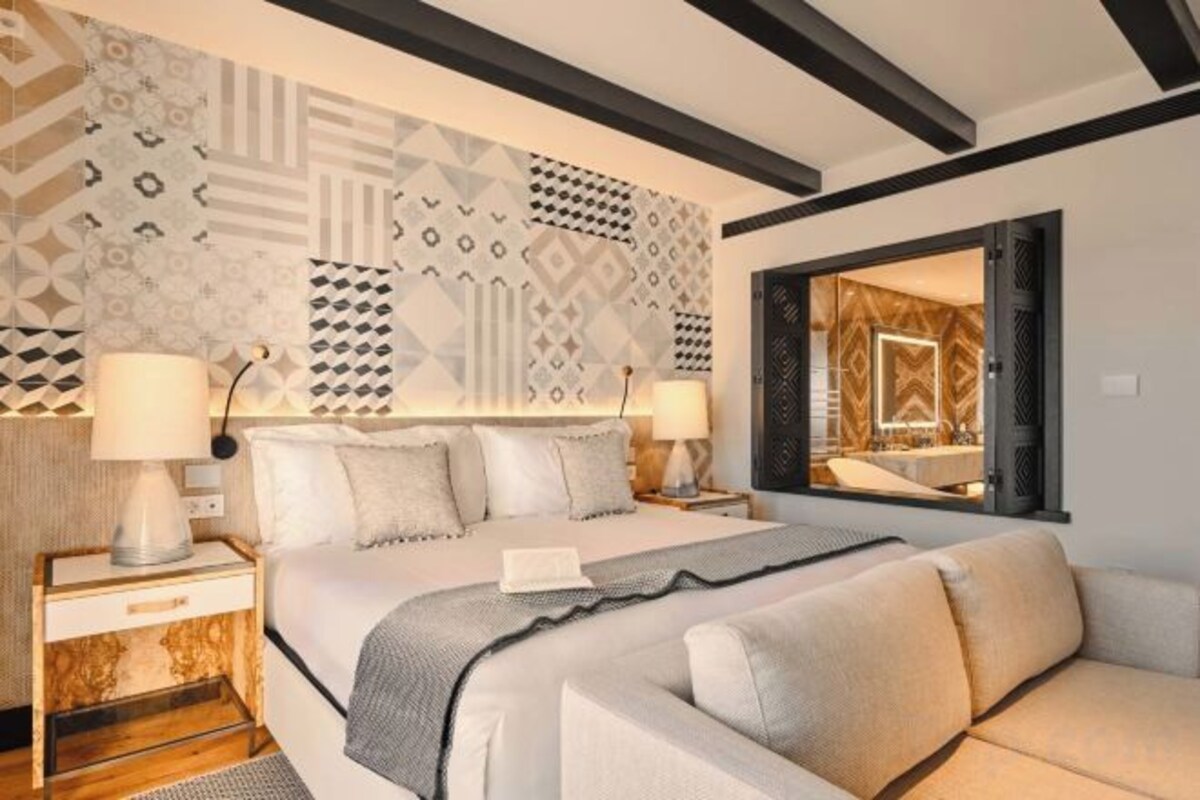 A hotel room with a large bed, two bedside tables, a sofa, and a patterned wall.