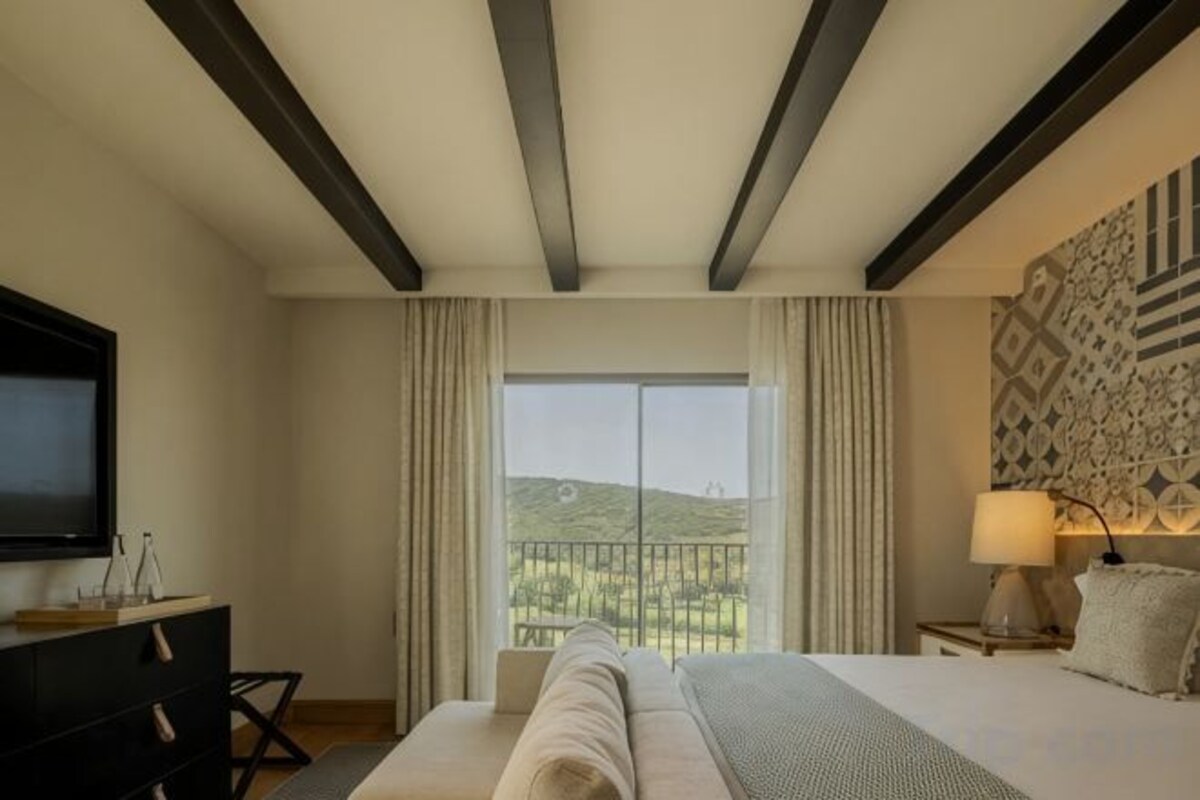 A hotel room with a bed, a TV, a desk, a lamp, and a view of a balcony.