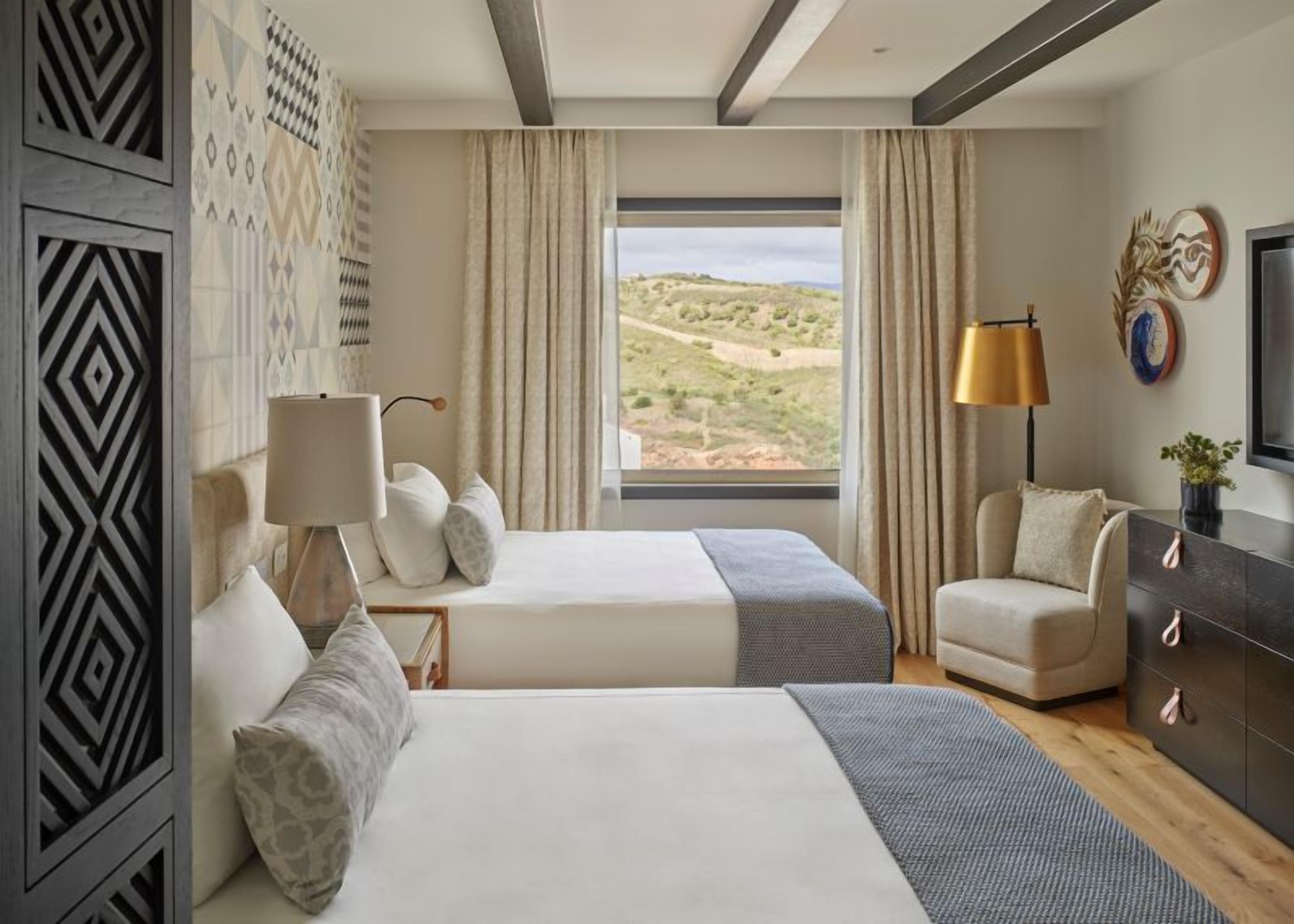 A hotel room with two beds, a sofa, a TV, and a large window with a desert view.