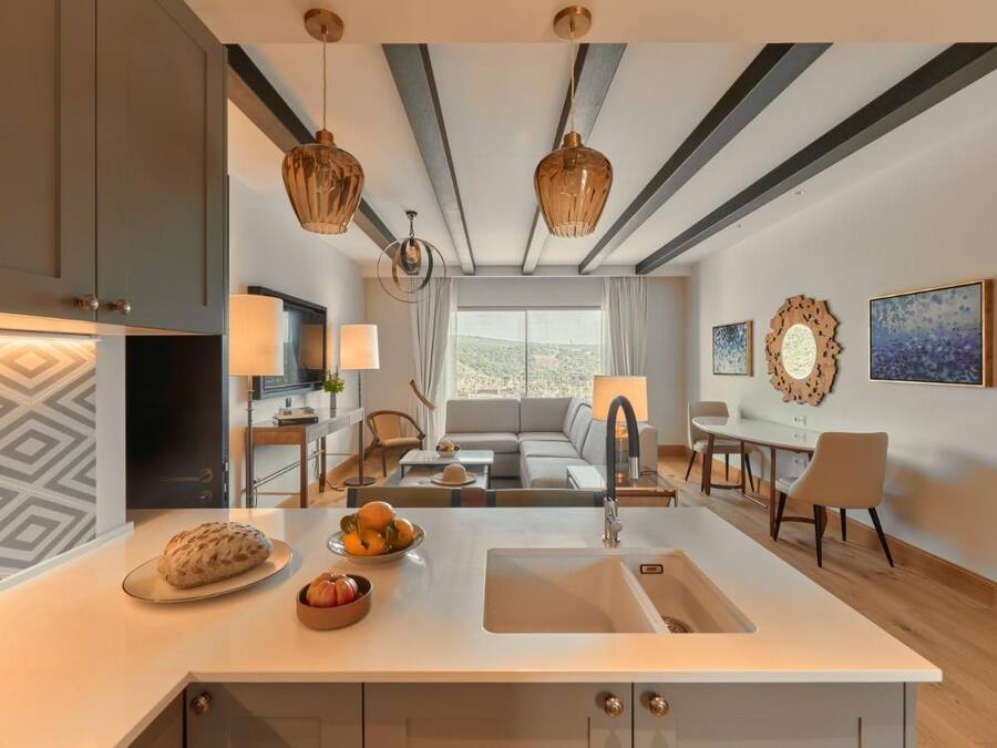 A modern kitchen with a central island, a dining area with a table and chairs, and a living room with a sofa and a view of the outdoors.