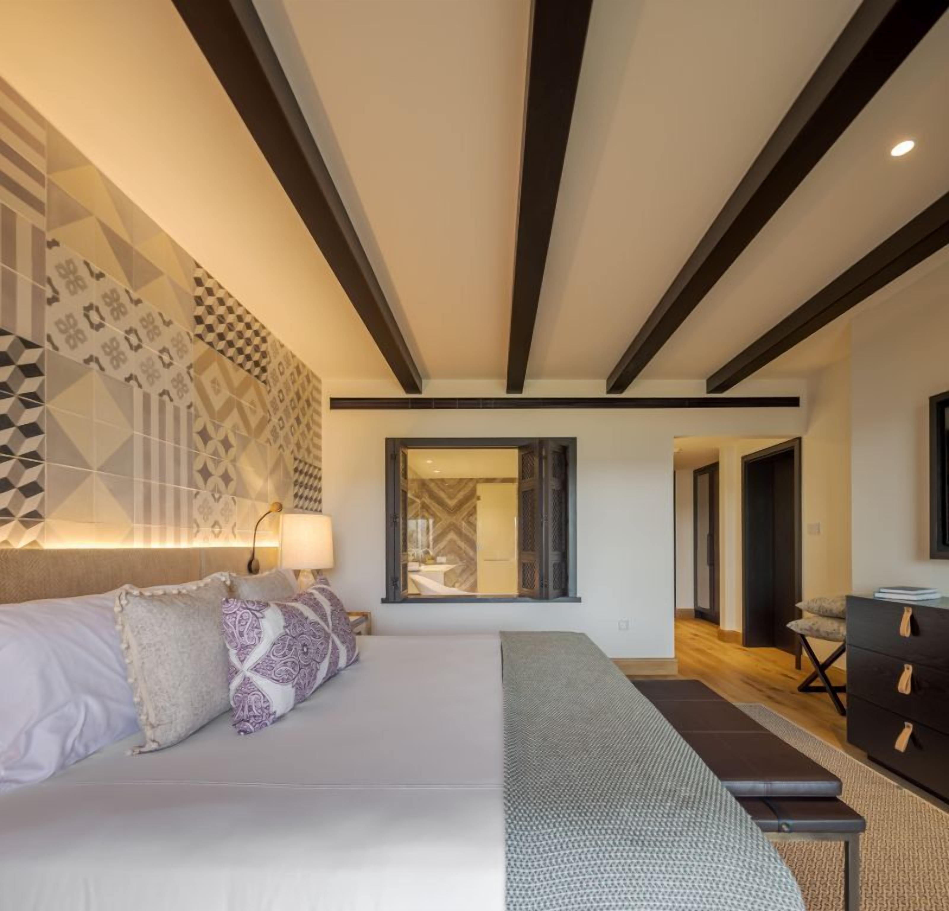 Ein modernes Schlafzimmer mit einem großen Bett, einer Bank, einer Kommode und einer Wand mit Muster.