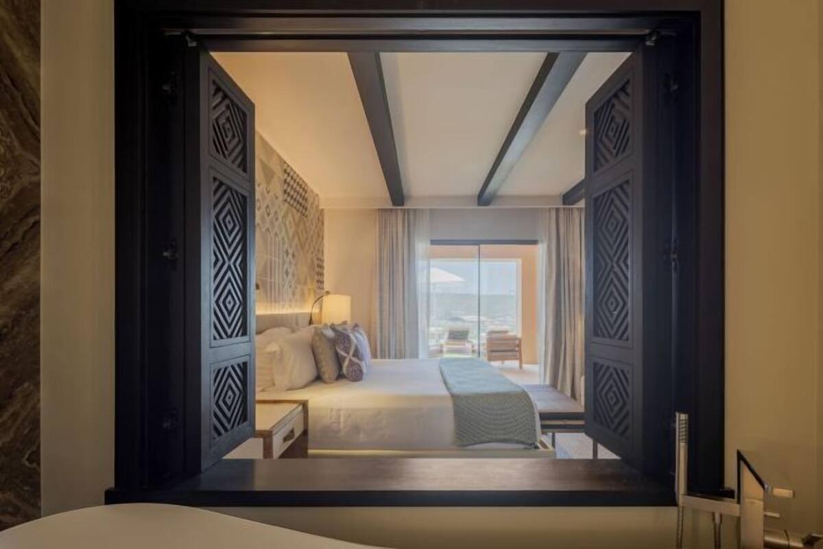A hotel room with a bed, bedside tables, a lamp, and a view of the ocean through large windows.
