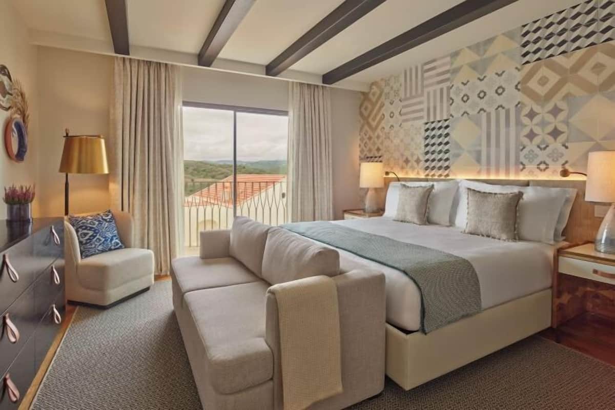 A hotel room with a large bed, a sofa, a desk, and a view of the outdoors.
