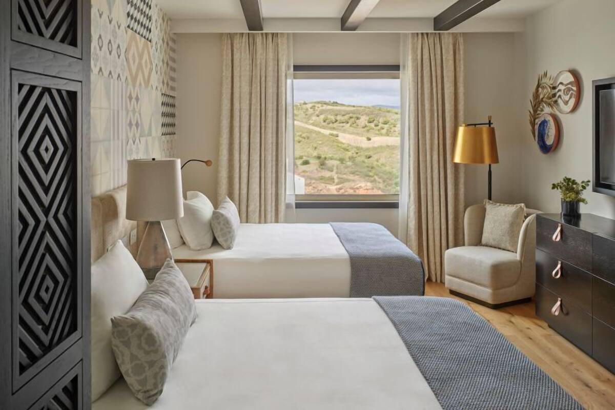 A hotel room with two beds, a sofa, a TV, and a large window with a desert view.