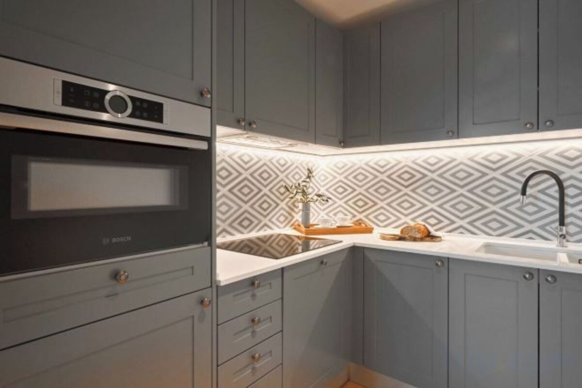 A kitchen with grey cabinets, a Bosch oven, a patterned backsplash, and a sink with a faucet.