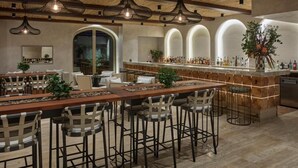 Un vaste espace dédié à la salle à manger, avec une longue table en bois, de nombreux tabourets de bar et des lampes suspendues.