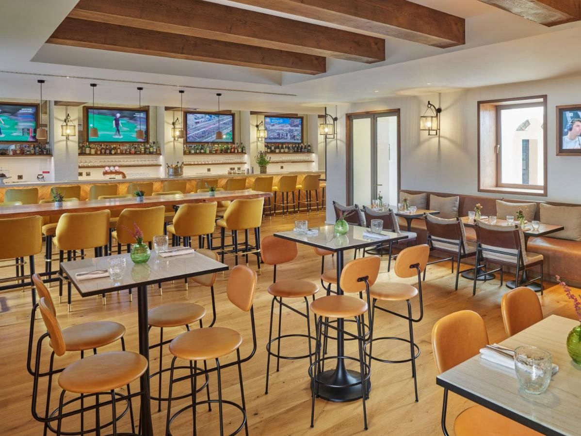A restaurant with wooden floors, yellow chairs, and tables. There are multiple TVs on the walls displaying sports.