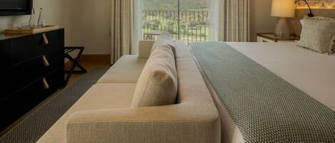 A modern hotel room with a large bed, a sofa, a TV, and a balcony with a view.