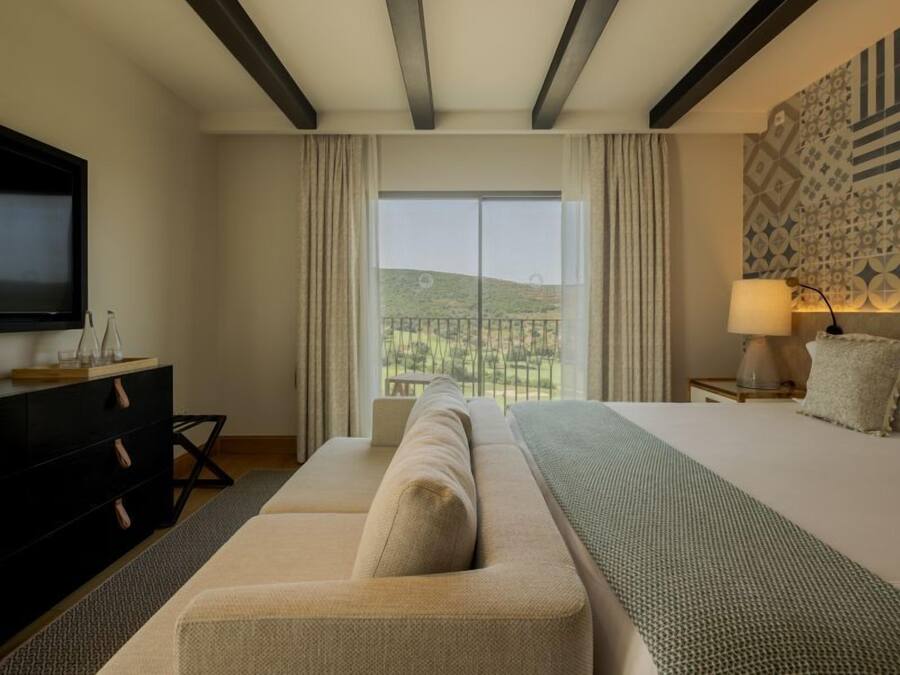 Quarto de hotel moderno com cama grande, sofá, televisão e varanda com vista.