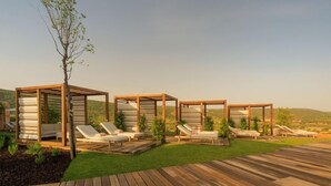 Une série de structures en bois dotées de coins salons intégrés, entourées d’une terrasse en bois et d’une pelouse verdoyante, le tout se détachant sur un ciel dégagé.