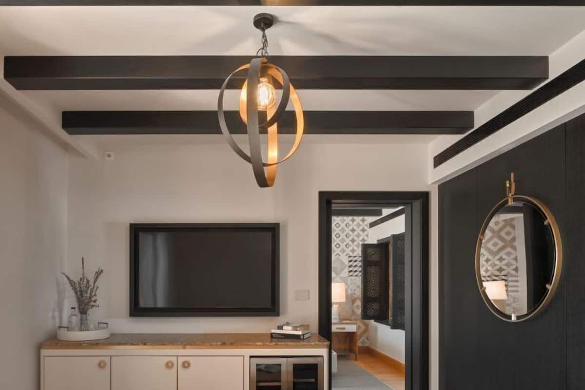 A modern living room with a flat-screen TV, a wooden bench, a bowl of fruit, and a unique pendant light.