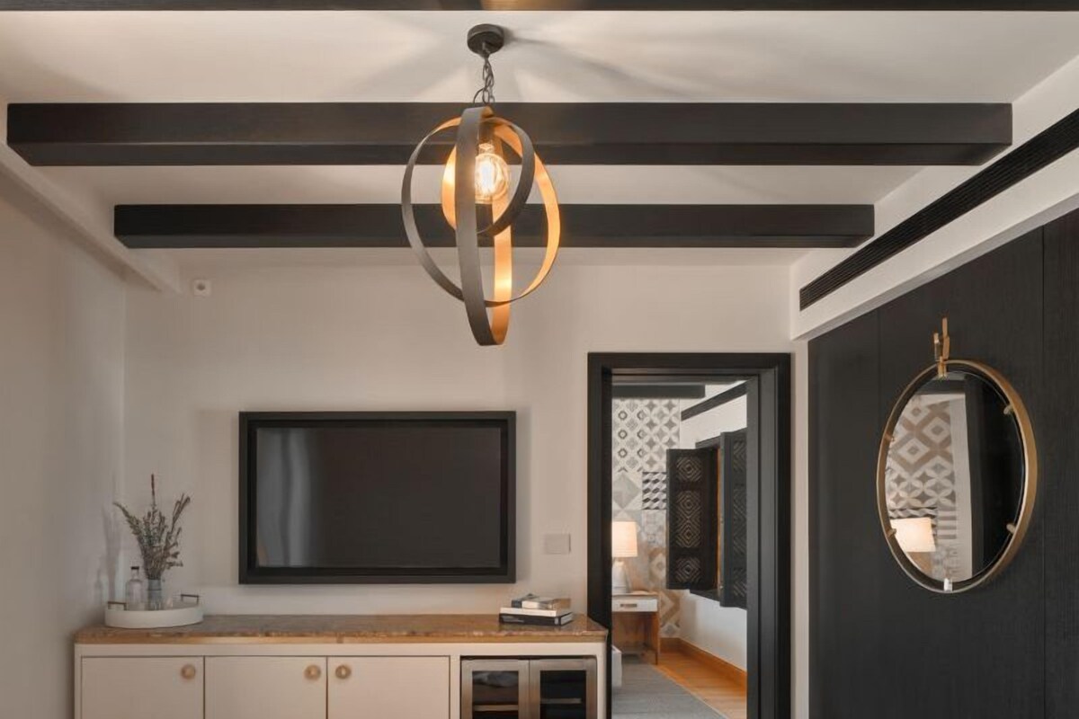 A modern living room with a flat-screen TV, a wooden bench, a bowl of fruit, and a unique pendant light.