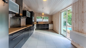 A modern kitchen with wooden walls, stainless steel appliances, and a large window overlooking a pool.