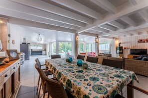 Un vaste espace dédié à la salle à manger, agrémenté d’une nappe à motifs, de meubles en osier et offrant une vue sur la cuisine et l’extérieur.