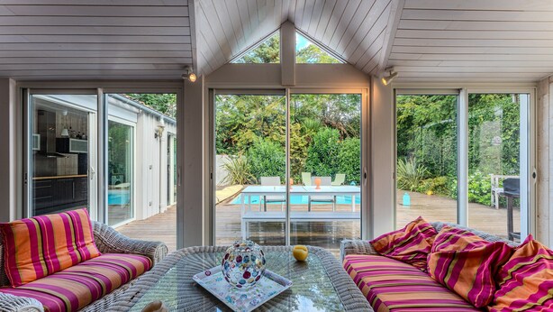 A sunlit room with a glass door leading to a pool, wicker furniture, and a decorative glass table.