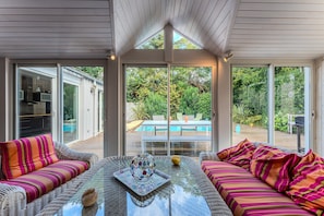 Une pièce baignée de lumière, avec une porte vitrée donnant sur une piscine, des meubles en osier et une table décorative en verre.