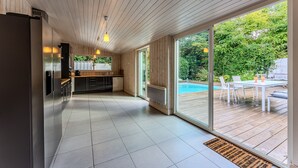A modern kitchen with a large refrigerator, a dining area with a table and chairs, and a view of a swimming pool through large sliding glass doors.