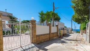 Une rue résidentielle avec une entrée fermée par un portail, une chaussée asphaltée et un ciel d’un bleu éclatant.