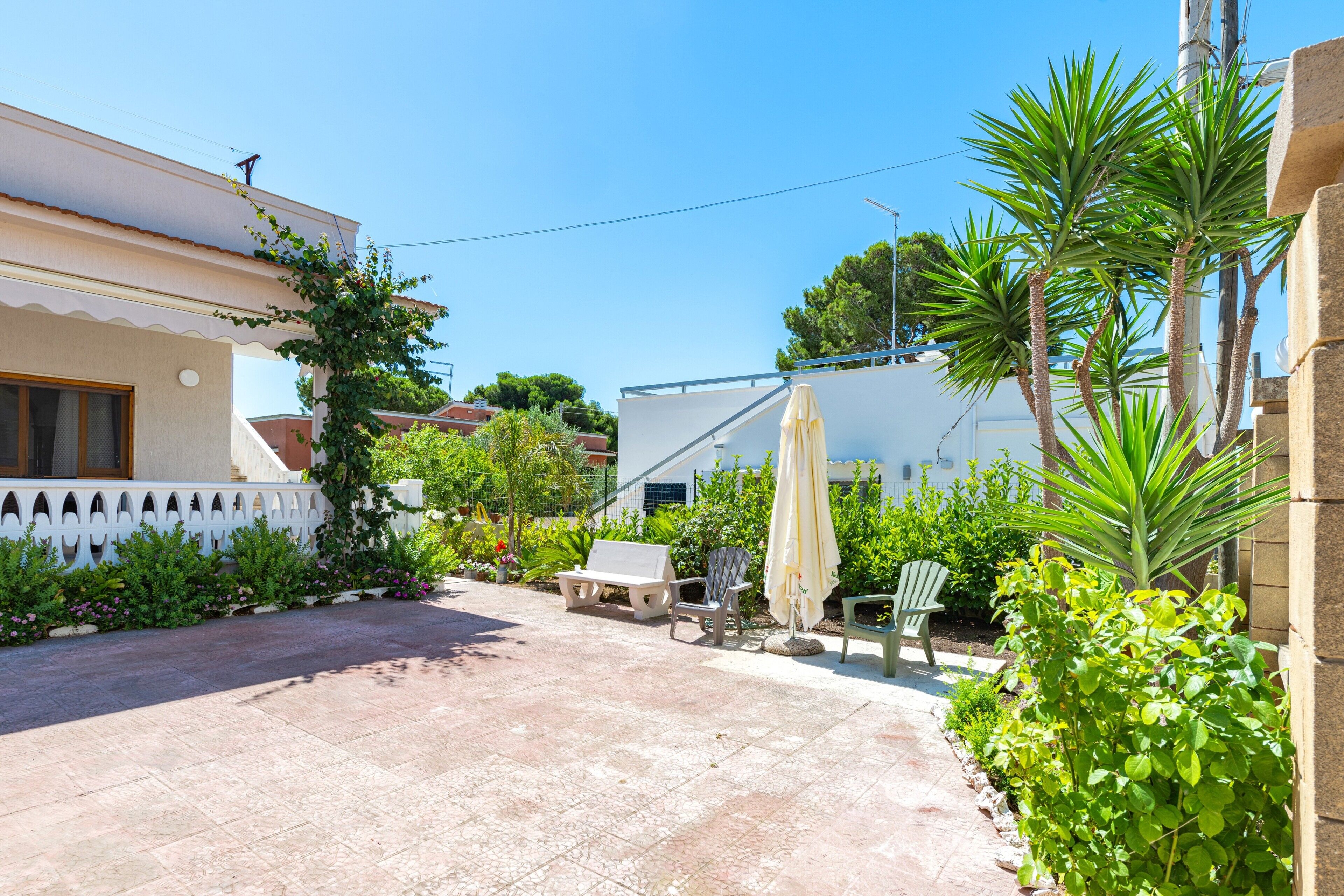 A patio with a white fence, a bench, a chair, and an umbrella.