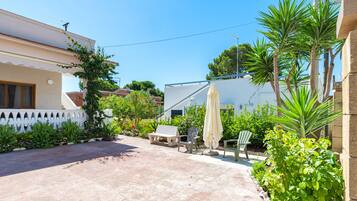 A patio with a white fence, a bench, a chair, and an umbrella.