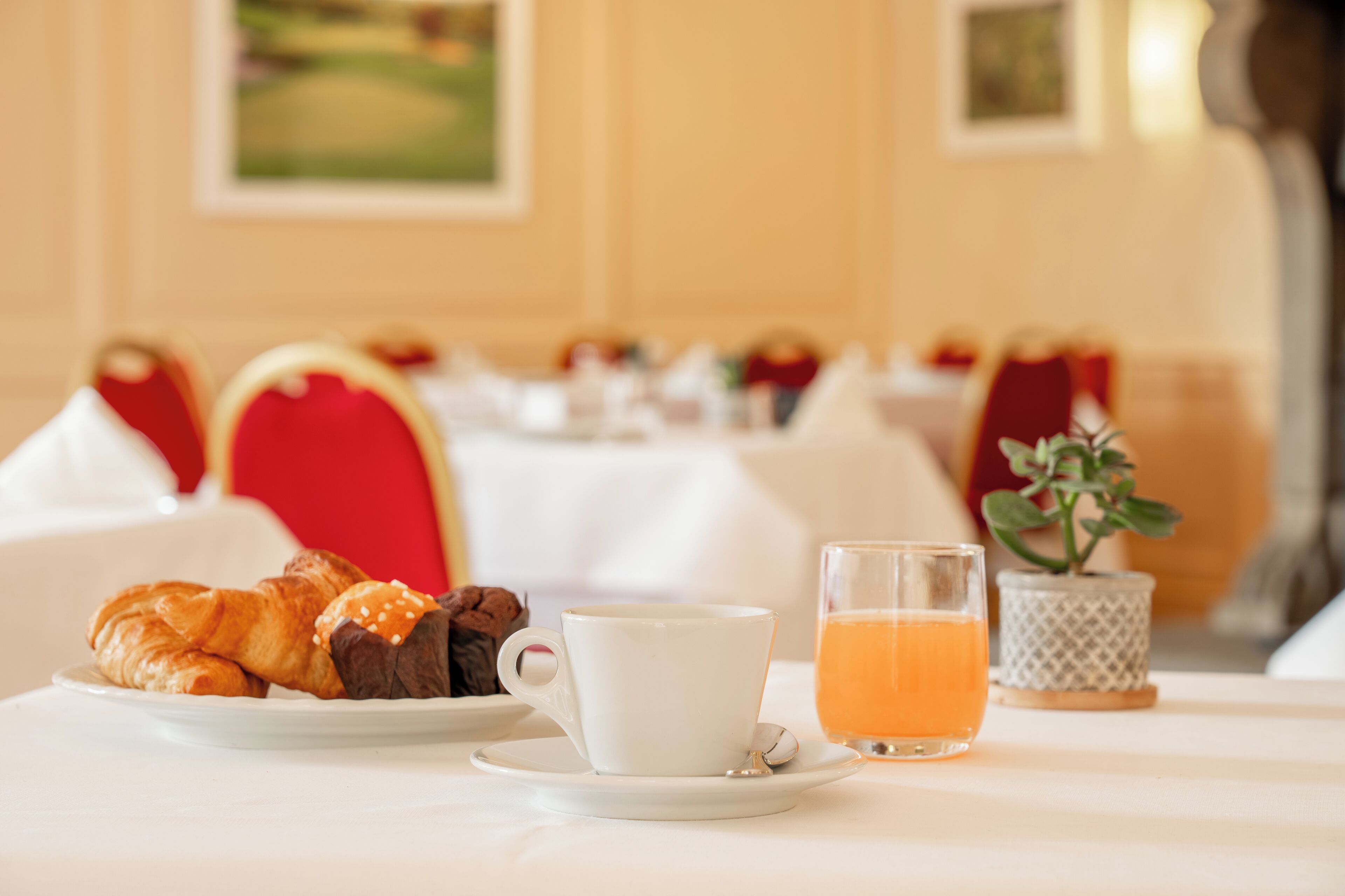 A breakfast setting with croissants, a cup of coffee, and a glass of orange juice on a table.