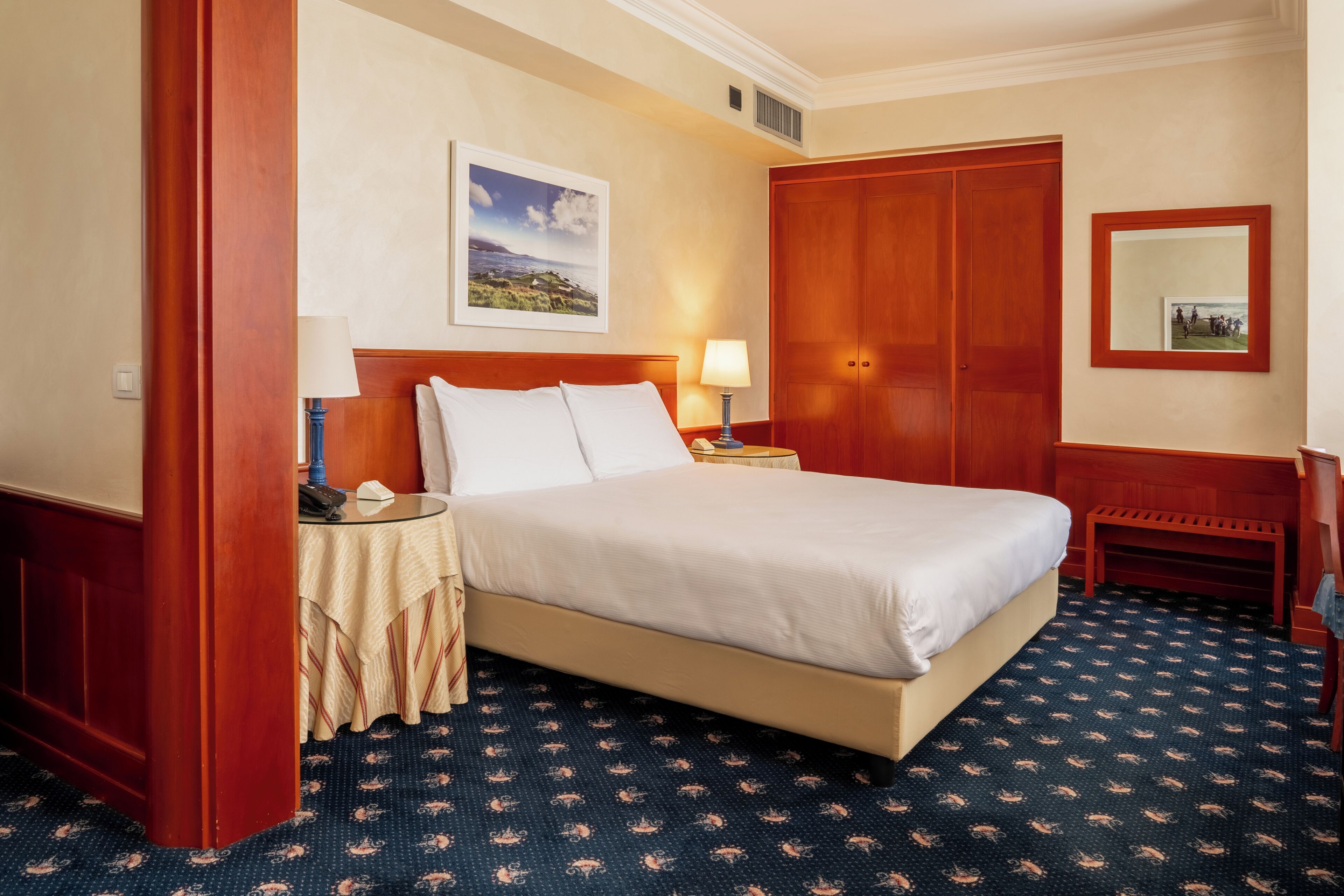 Une chambre d’hôtel avec un lit, une table de chevet, une lampe et un grand miroir.
