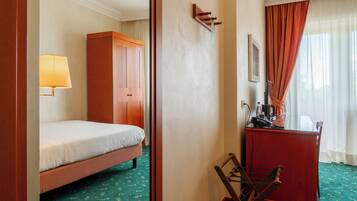 A hotel room with a bed, a desk, a chair, a lamp, and a wardrobe.