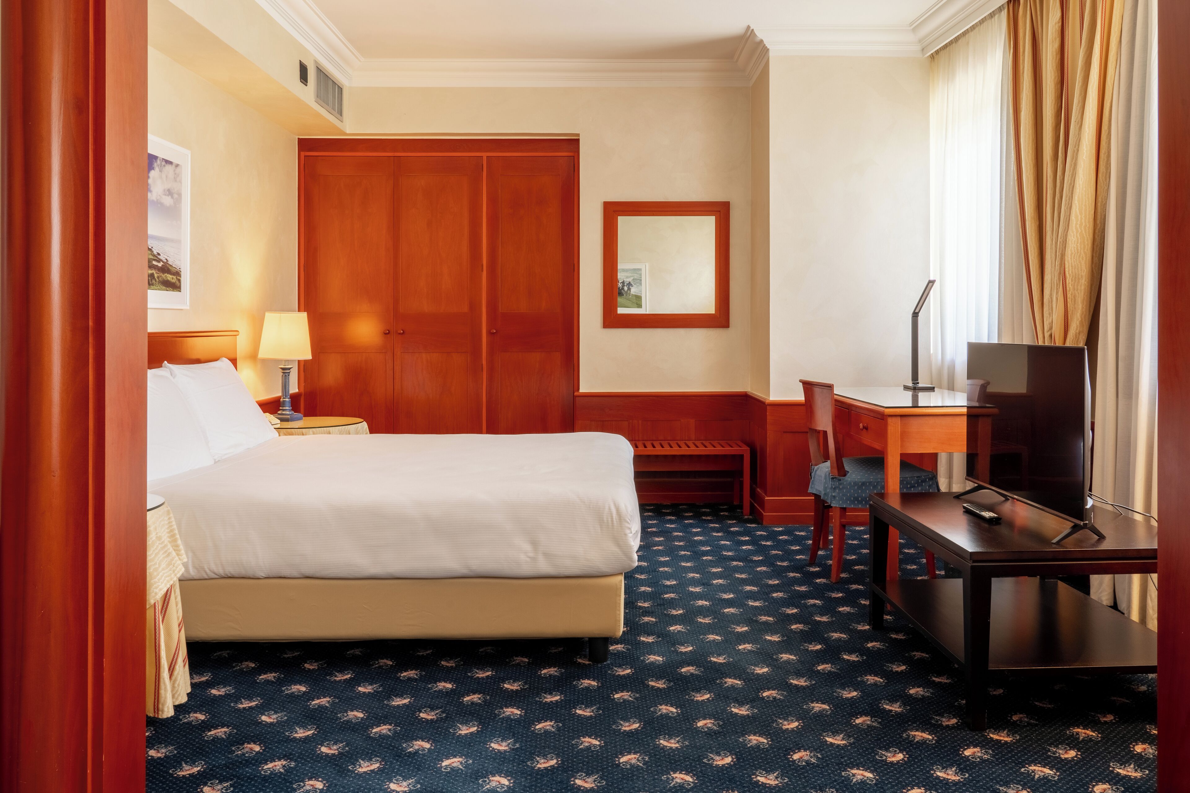 Una habitación de hotel con cama, escritorio, silla, televisor y armario.