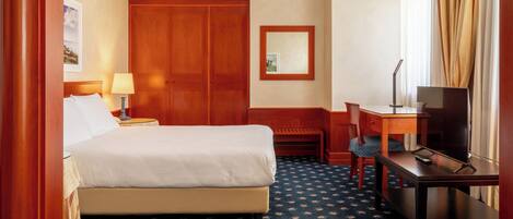 Una habitación de hotel con cama, escritorio, silla, televisor y armario.