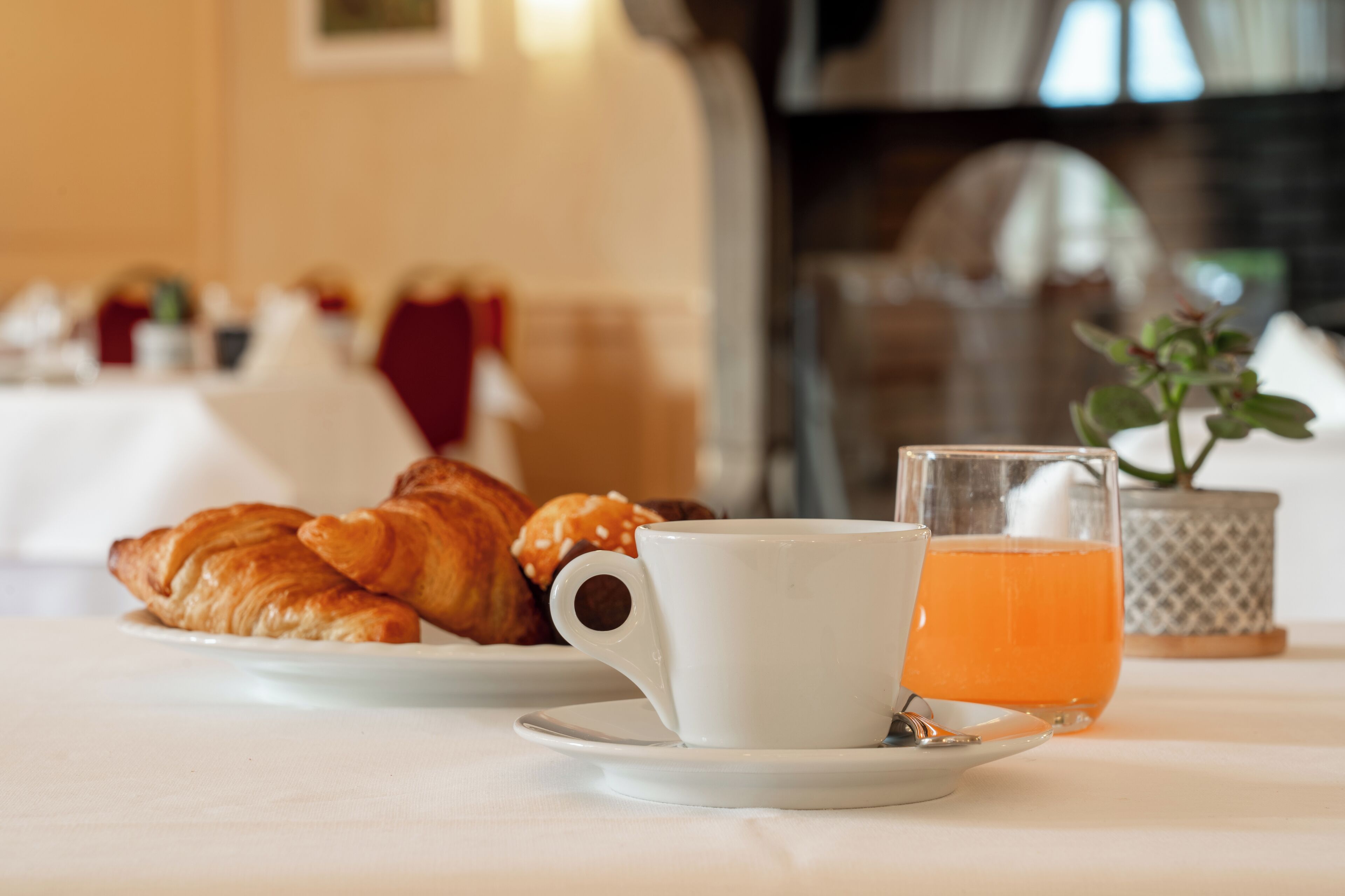 Un desayuno con cruasanes, una taza de café y un vaso de zumo de naranja sobre una mesa.