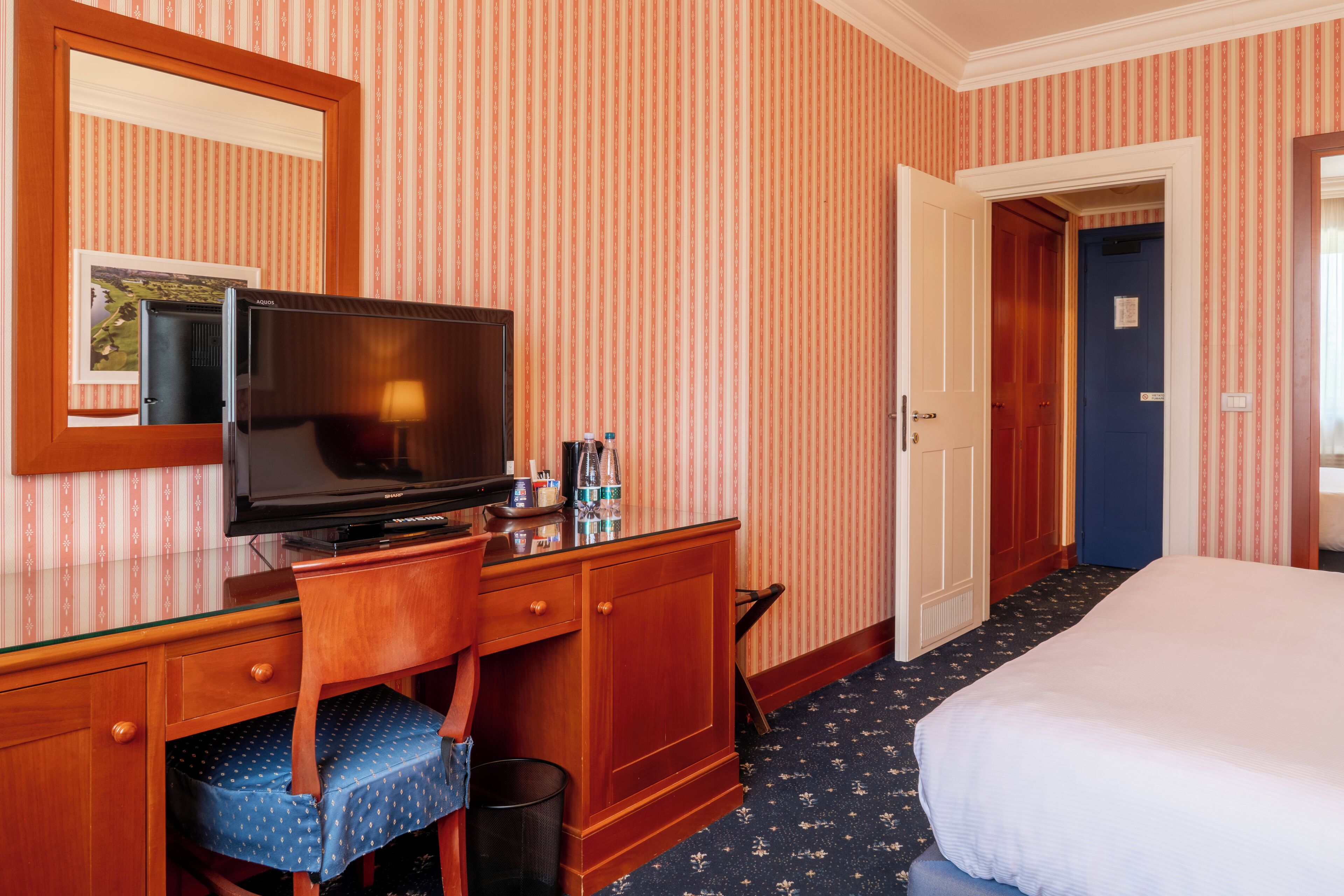 Ein Hotelzimmer mit einem Holztisch, einem Fernseher, einem Sessel, einem Bett und einer Tür zu einem weiteren Raum.