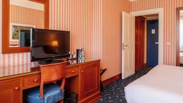 Ein Hotelzimmer mit einem Holztisch, einem Fernseher, einem Sessel, einem Bett und einer Tür zu einem weiteren Raum.