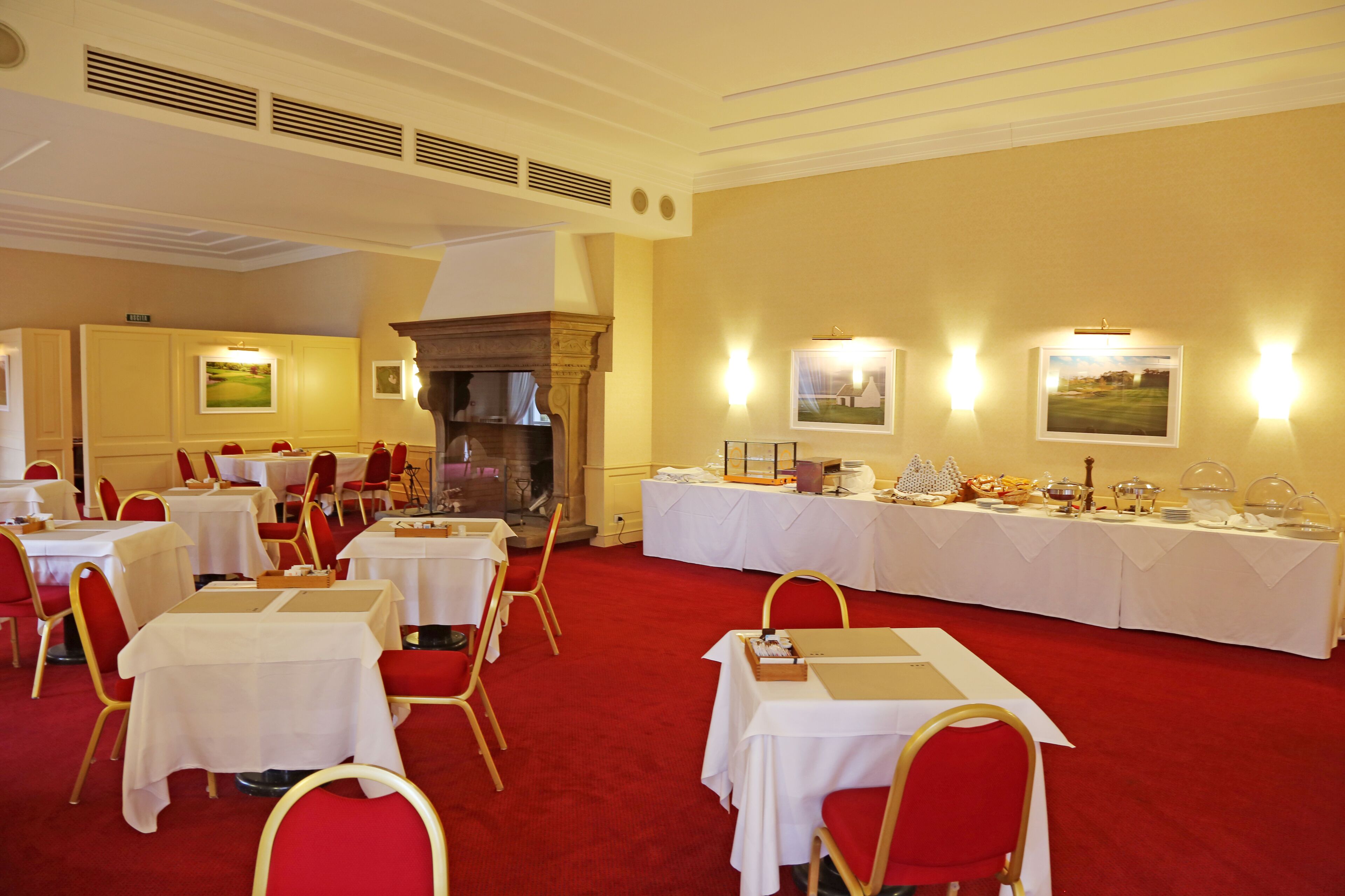 A banquet hall with tables set for a formal event, featuring a red carpet and white tablecloths.