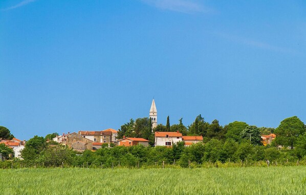 Paisatge rural amb una torre d'església destacada, envoltat de cases amb teulades vermelles i un camp en primer pla.